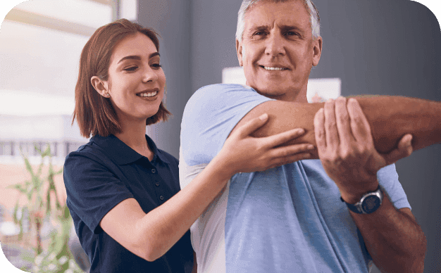 A young female physiotherapist assists an older male patient in a mobility exercise, helping him stretch his arm.